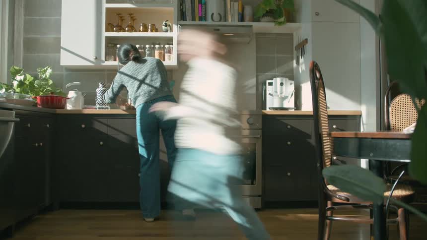 Mother and daughter moves around in the kitchen at daytime