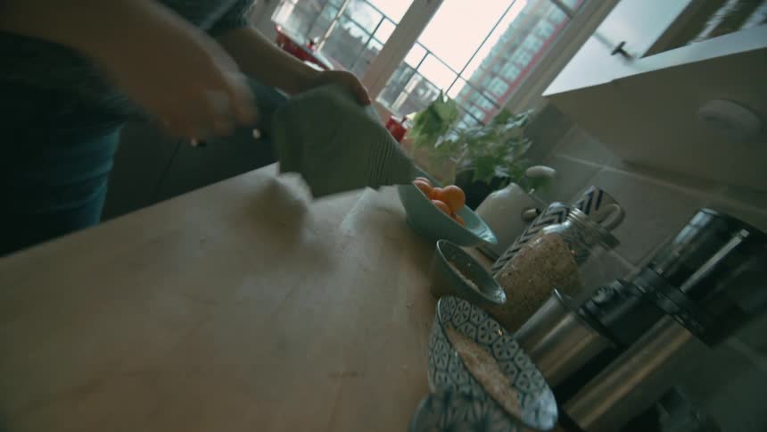 A woman picks up a napkin from the countertop and cleans the top of the stove in the kitchen at midday