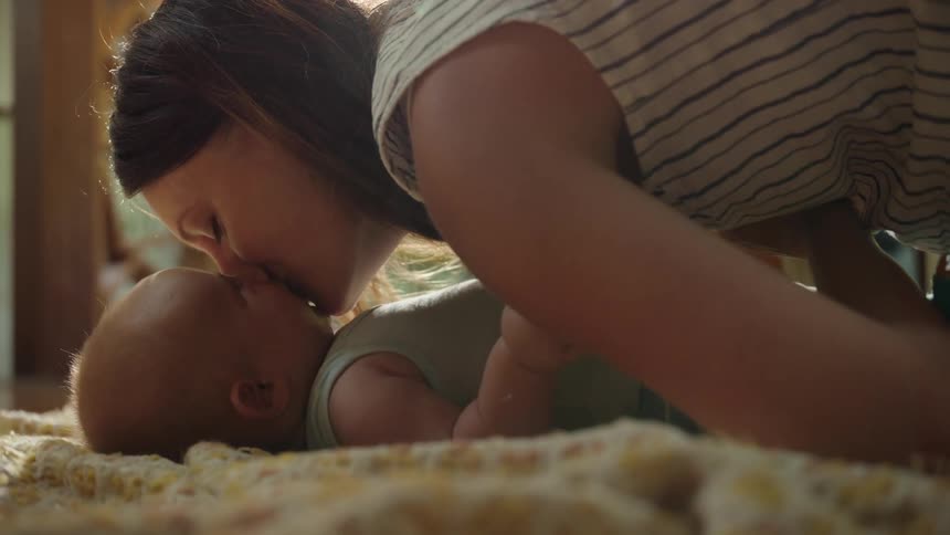 Mother kissing baby lying on rug