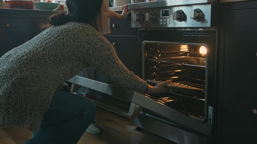 A woman and her daughter place cookies into the oven for baking in the kitchen at midday