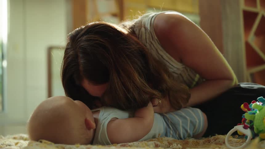 A mother is playing with her infant son while sitting on the living room floor