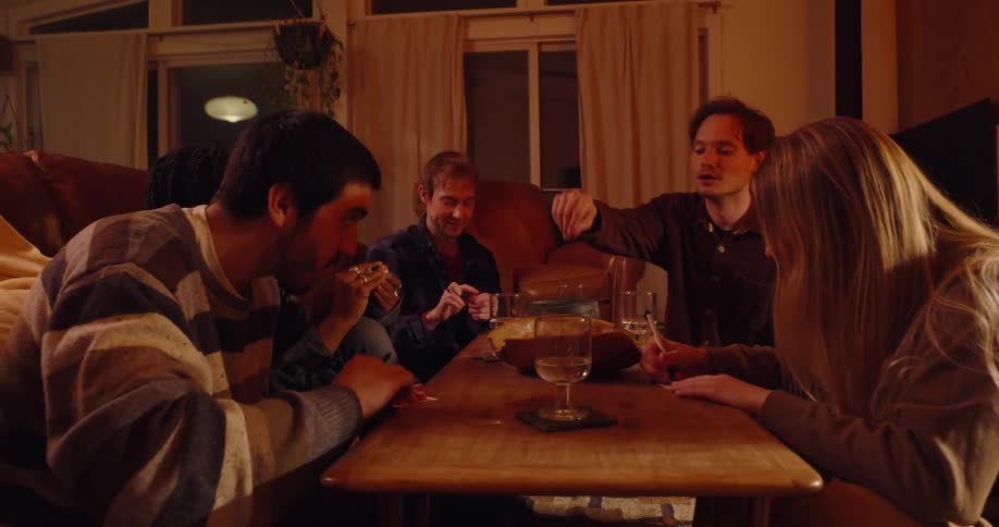 A group of friends write into white cards and drop them in a bowl on a table in a living room