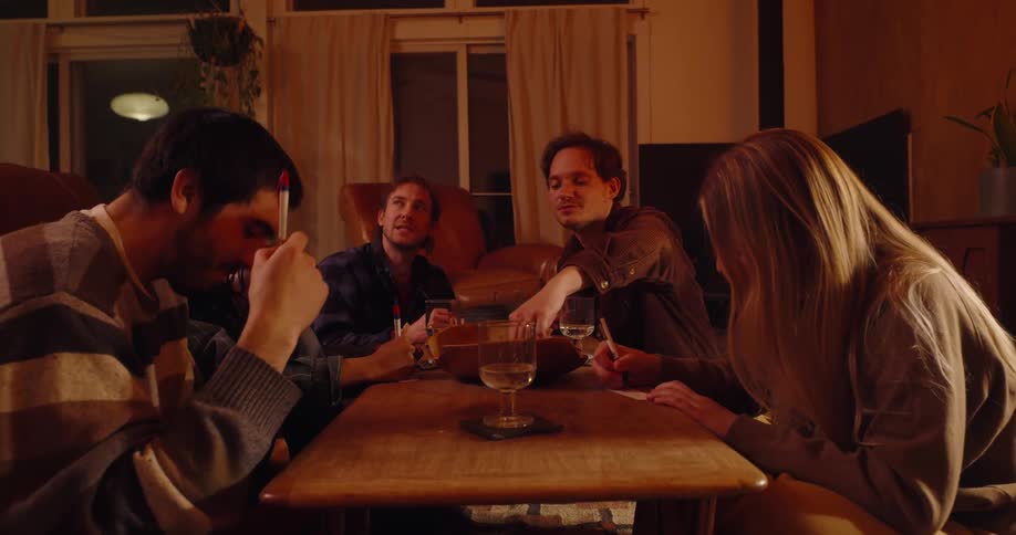 A group of friends are gathered around a table eating and drinking in a warmly lit room
