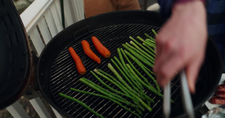 A man is putting food on a grill as other people mingle on a deck
