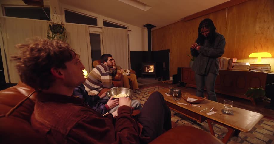 In a cozy dimly lit living room warmed by a woodburning stove a group of friends animatedly play charades