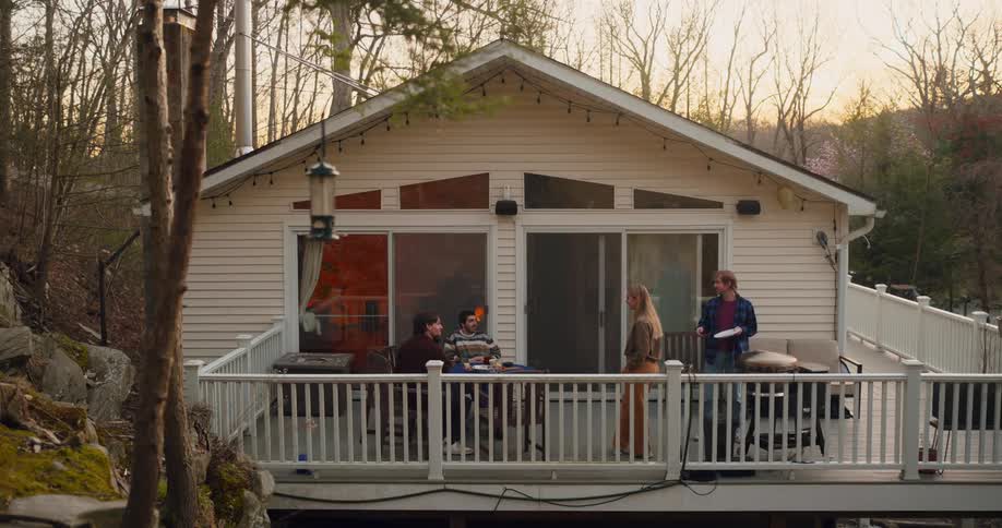 A white singlestory house with large windows and a deck with several people gathered outside