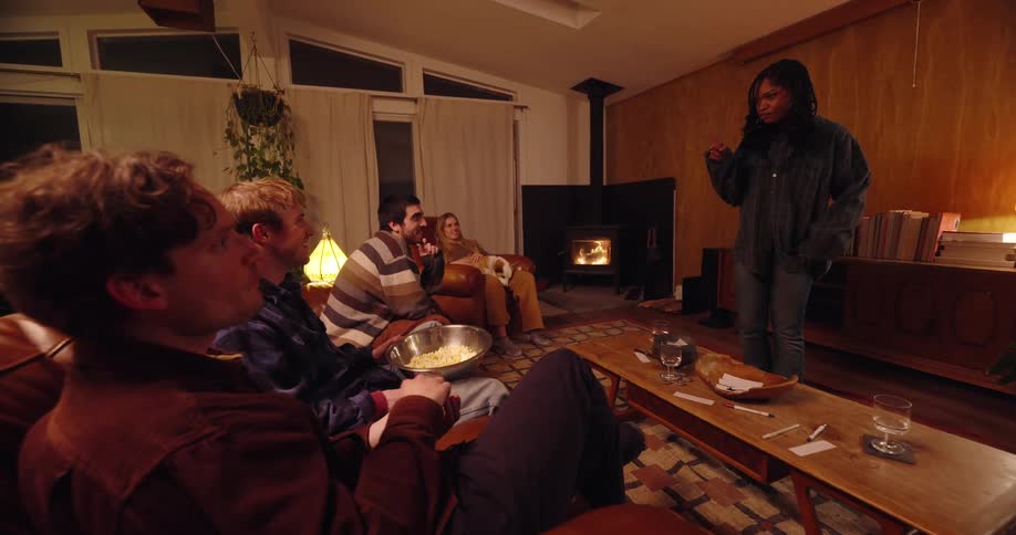 Woman standing playing charades while her friends sit eating popcorn trying to guess