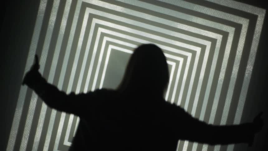 Woman appears to walk down a tilted hallway with flashing lights