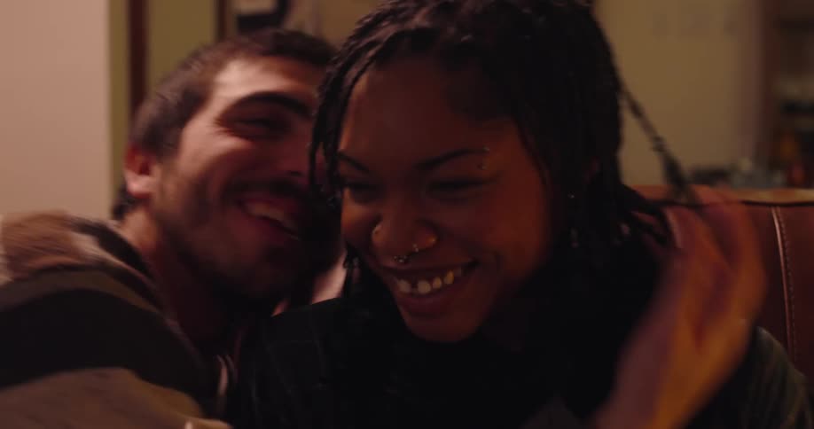 A young couple sits on the couch as the man kisses the woman on the cheek