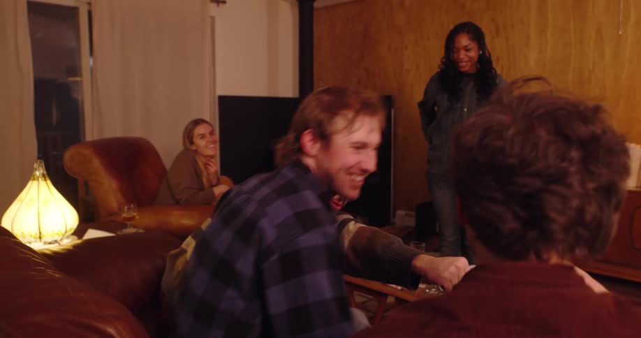 Group of smiling friends sitting in living room with woman standing