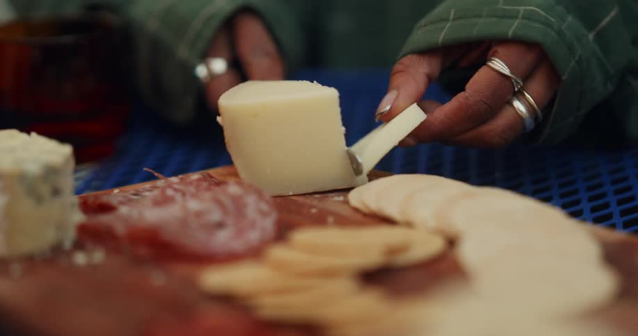 Pair of hands cutting a slice of cheese on a charcuterie board on the table