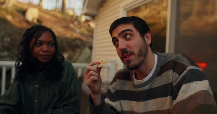 Man eating cheese and crackers from a charcuterie board while hanging out with friends outdoors