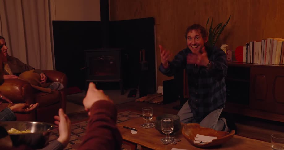 Friends sitting on a couch in the living room playing charades while eating popcorn