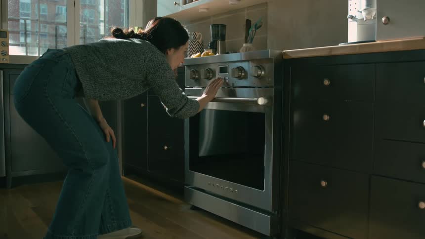 Woman operates an electric oven in a kitchen and leaves shortly after