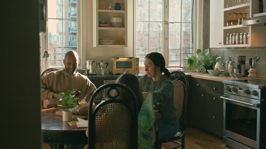 A man a woman and a child sitting at the kitchen table talking eating and drinking