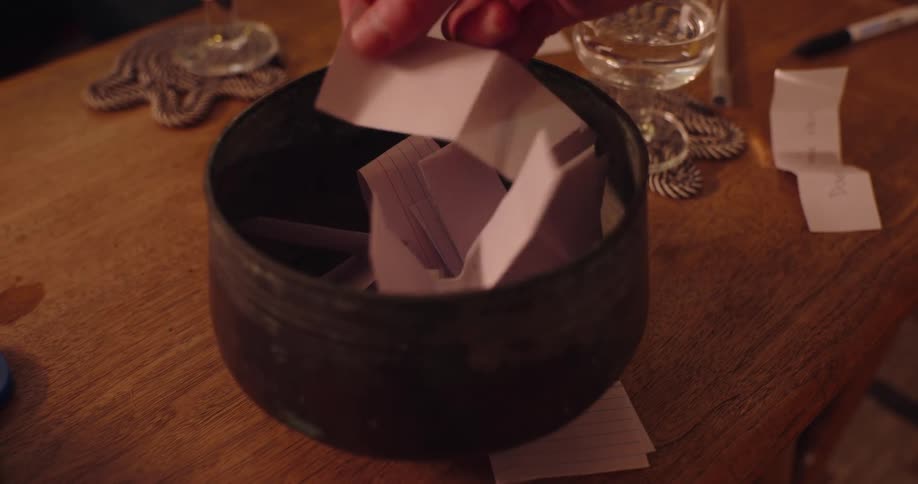 A person fumbles through a bowl with folded paper and chooses one