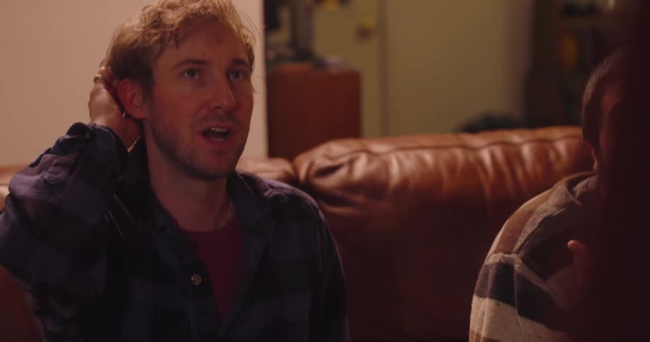 Two friends sitting on a couch looking forward with observing another person and interacting