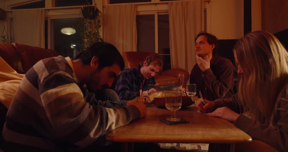 Group of friends sitting in a living room and writing on white papers