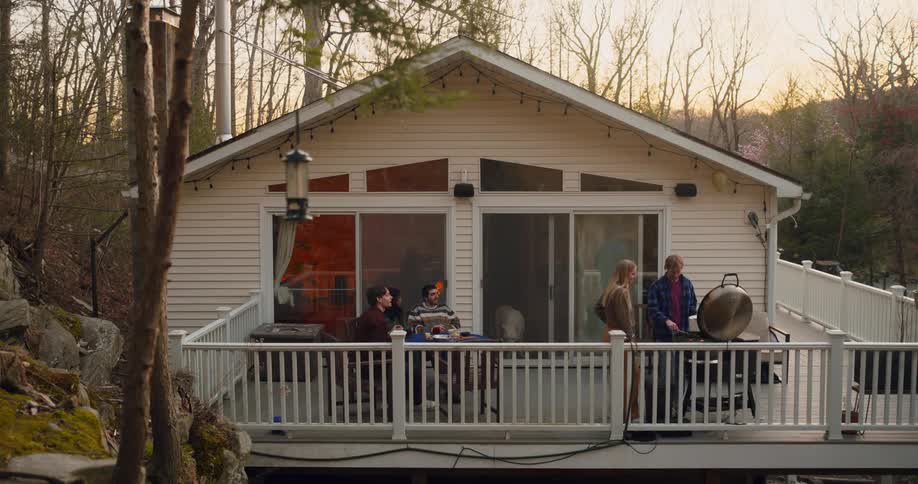 Group of friends sitting at a table and others having a barbecue in a leisure moment in a house in the forest