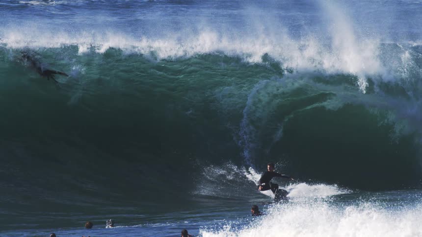 Several people on a wave in the ocean with one of them surfing