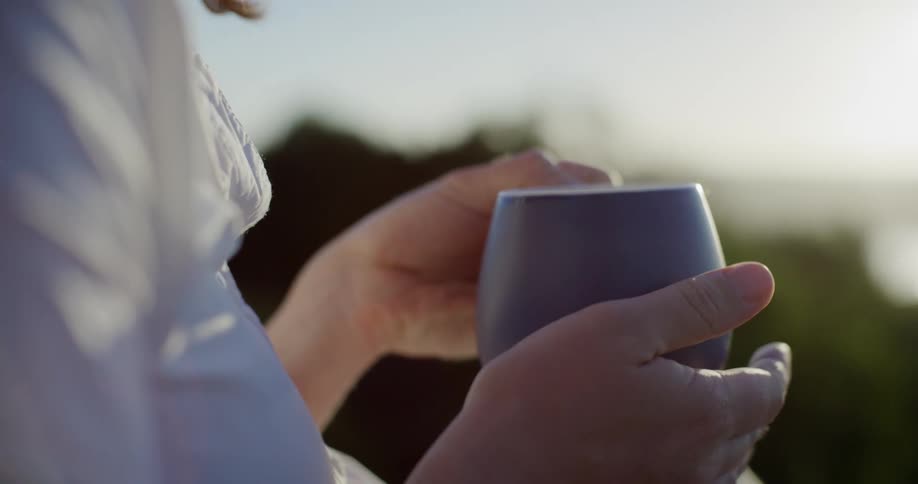 Closeup of a woman holding a cup containing hot liquid and raising it to sip