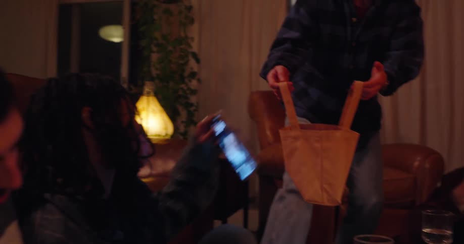A small group of friends sit on the living room floor and put their smartphones into a bag