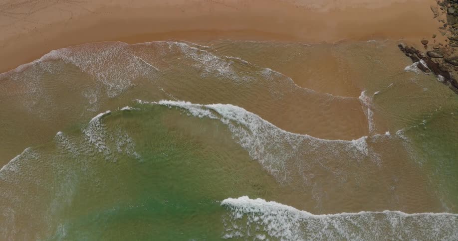 Aerial view of greenish waters with gentle waves reaching the sand of the beach