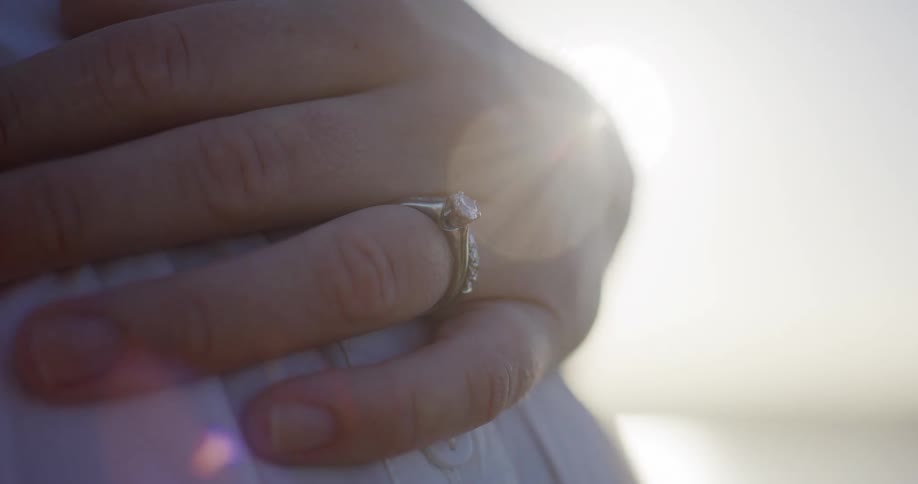 Sun glisenting on womans wedding ring as her hand is resting on pregnant belly