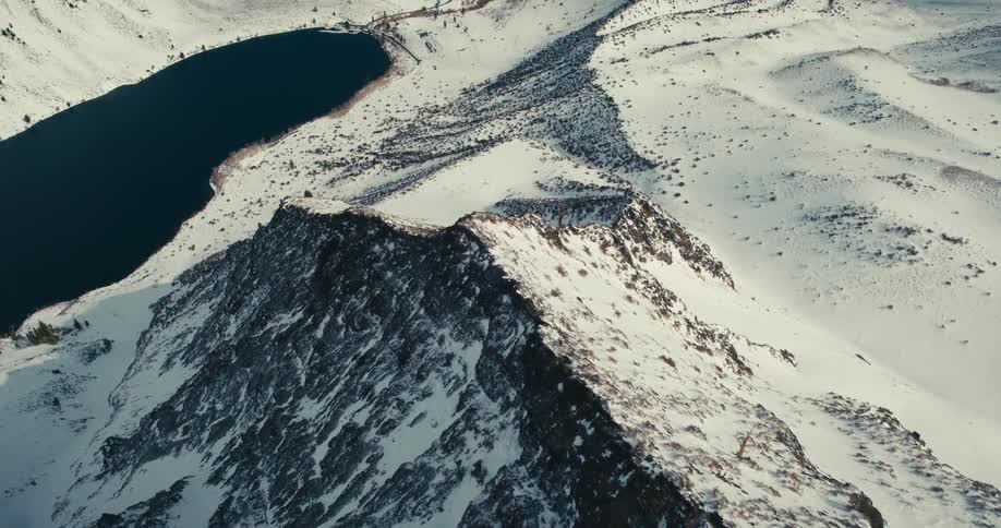 Aerial view of snow cover on a mountain ridge and a lake at the foot of the mountain