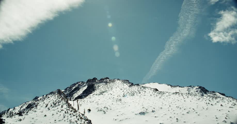 Time lapse of white clouds rolling over mountain summit covered in snow on a bluebird day