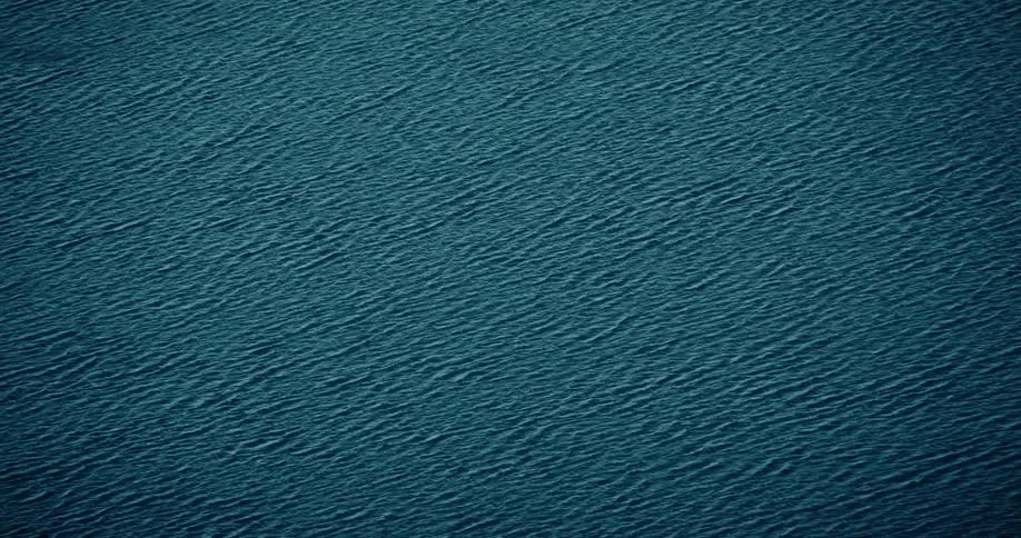 A continuous aerial topdown shot shows a vast expanse of tealcolored water with a mesmerizing pattern of gentle consistent ripples moving across its surface