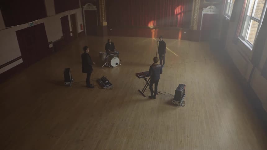 A band of musicians plays in an empty hall with red curtains