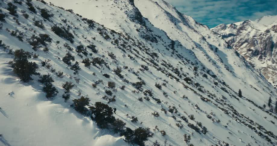 Aerial shot of two people climbing a mountain covered in snow and sparse vegetation