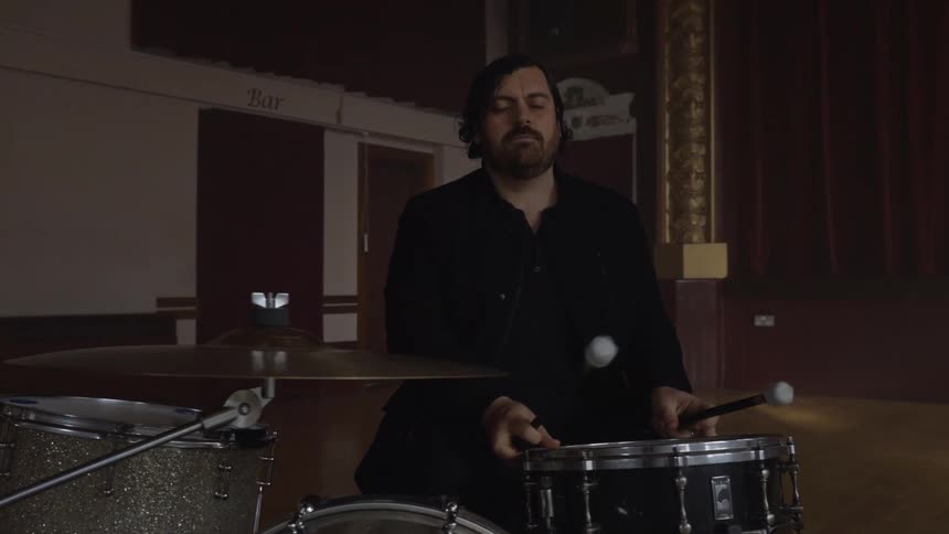 Man walking into an empty hall and sitting in front of his musical instrument and starting to play drums
