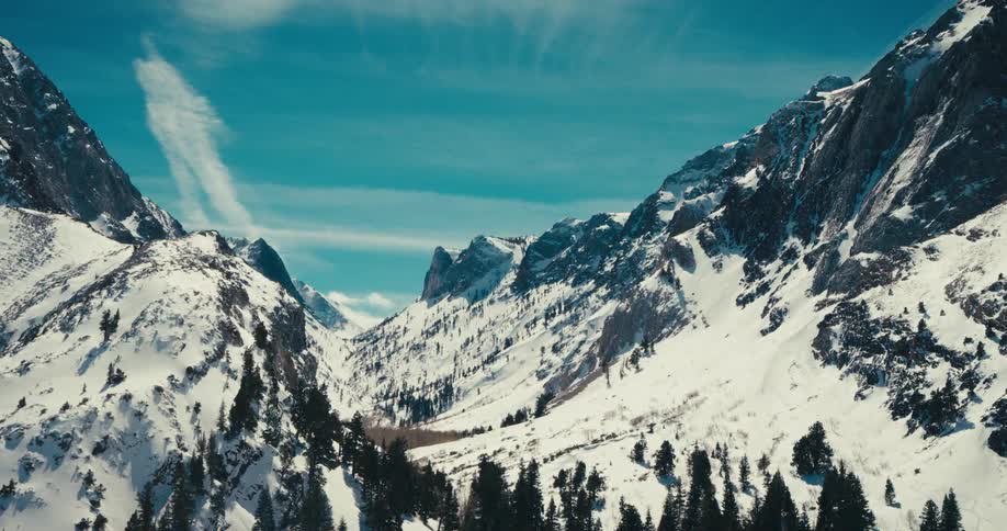 Snowcovered mountains rise under a bright blue sky with wispy clouds