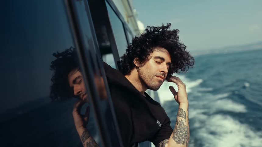 Man hanging out the window of a moving yacht looks around on a sunny day