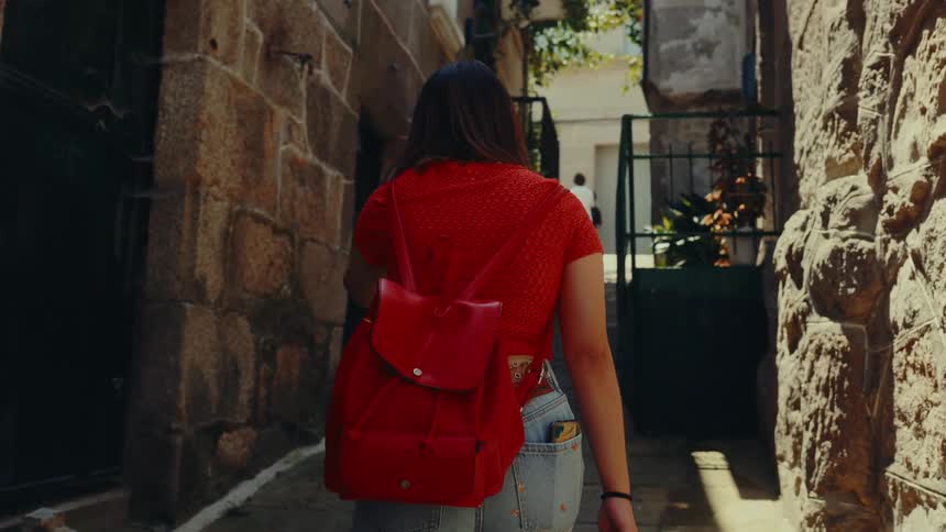 Woman with a red backpack on her back walking through an urban neighborhood with classical architecture
