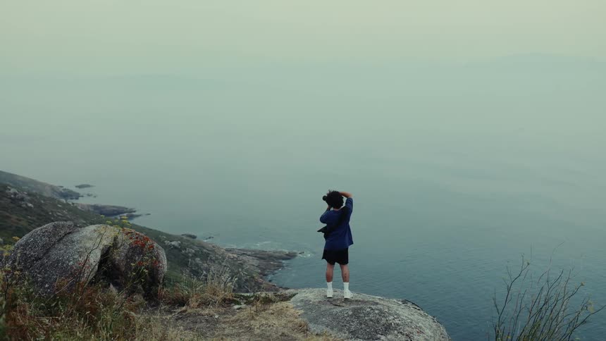 Person on a cliff rock by the sea taking a photo