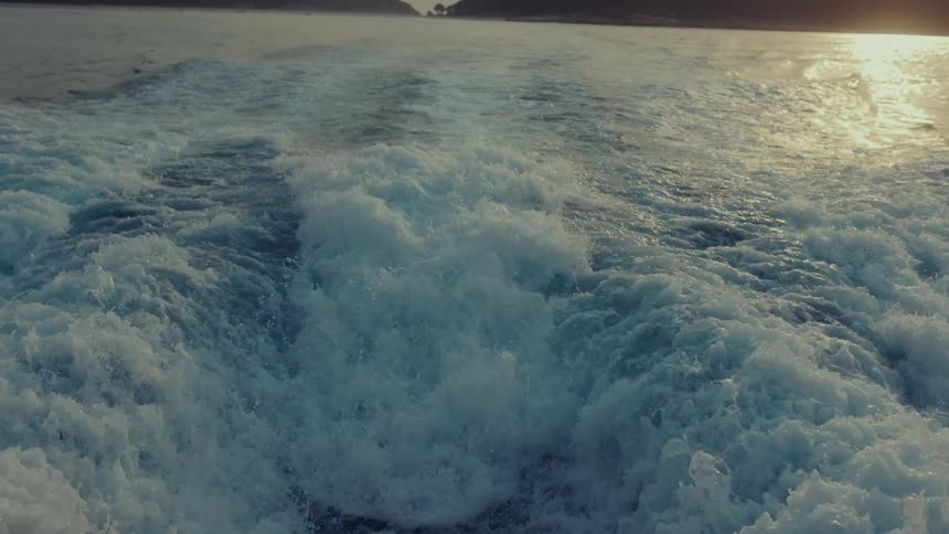 Close up of propeller waves on the ocean surface from behind a moving boat at dusk