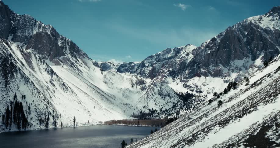 A breathtaking wide angle view of a snow covered mountainous landscape with steep rocky peaks surrounding a serene alpine lake