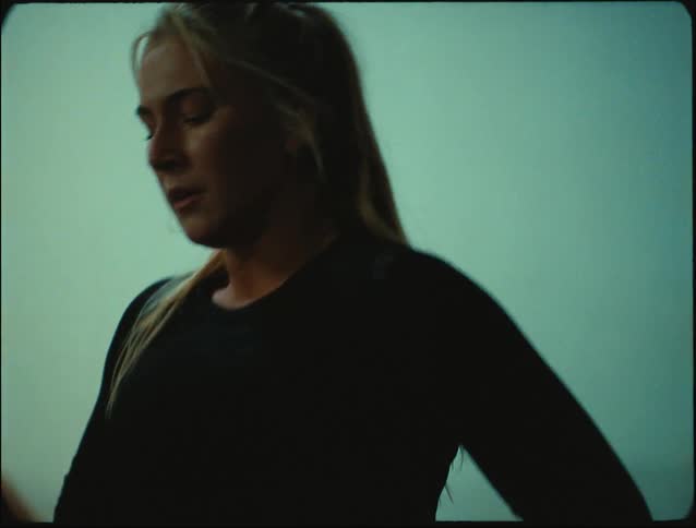 A woman stands up visibly winded inside of a gym with other people sitting