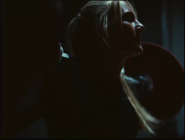 A woman in a dimly lit gym strains with determination while lifting a heavily loaded barbell across her shoulders