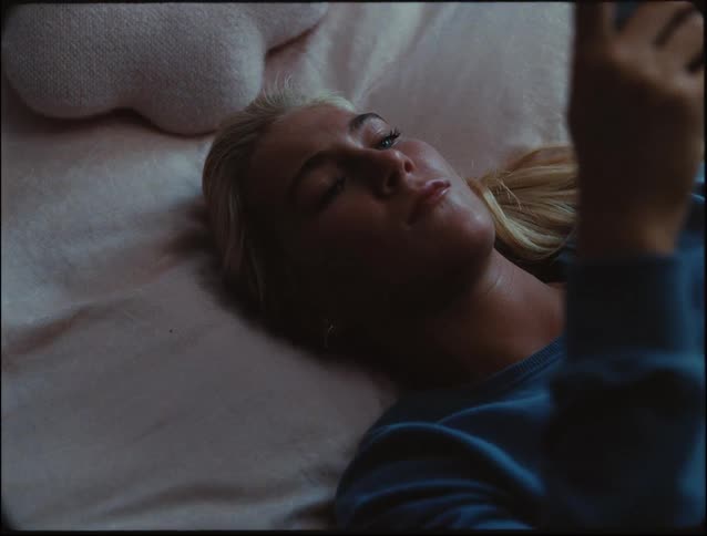A woman lying on a bed looking at her phone and staring at it