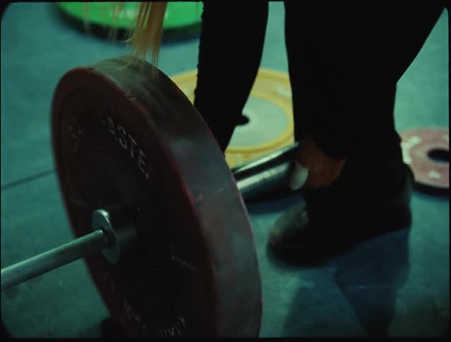 A woman is preparing to lift a barbell loaded with heavy weight plates in a gym setting