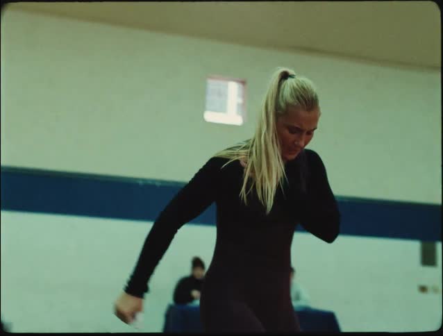 A woman in a gym lifting weights feeling a shoulder injury as she drops the weight while two men sit nearby watching