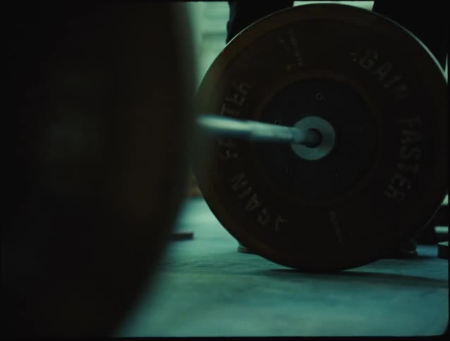 A person is preparing to lift a loaded barbell in a dimly lit gym setting focusing on strength and discipline