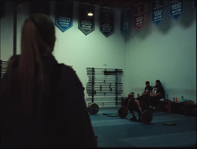 Lady lift weight inside the gym at night with others watching