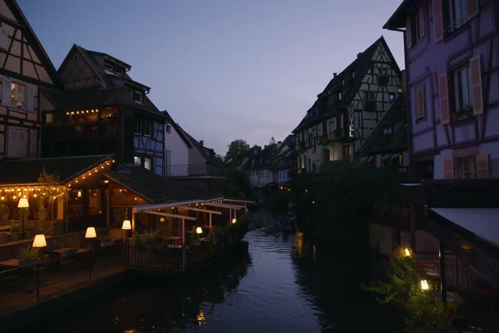 A boat glides down a canal past charming illuminated buildings in a european town at dusk