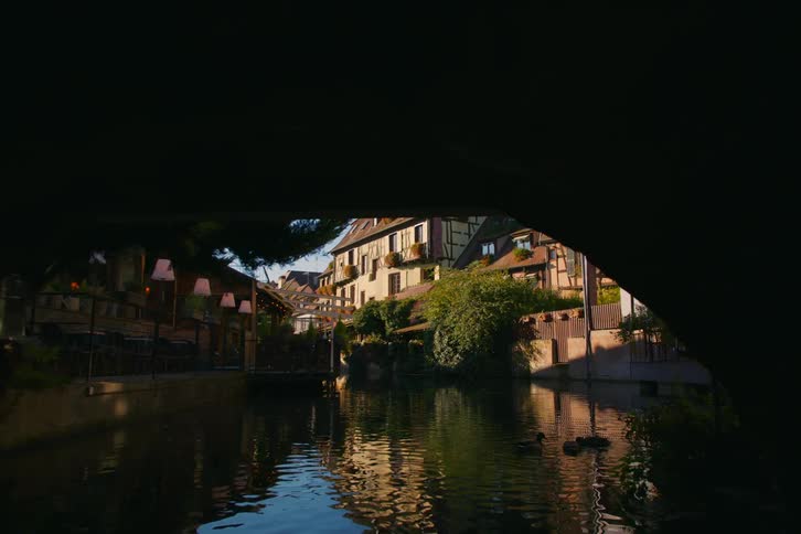 A serene canal winds through a charming european village with timber framed houses and outdoor cafs lining the waterway