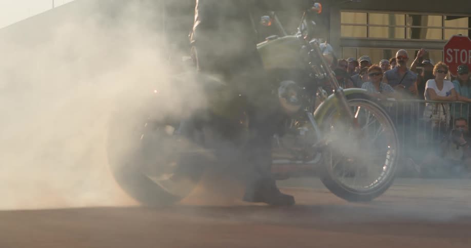 A motorcycle blows out smoke as a man stands and rotates it